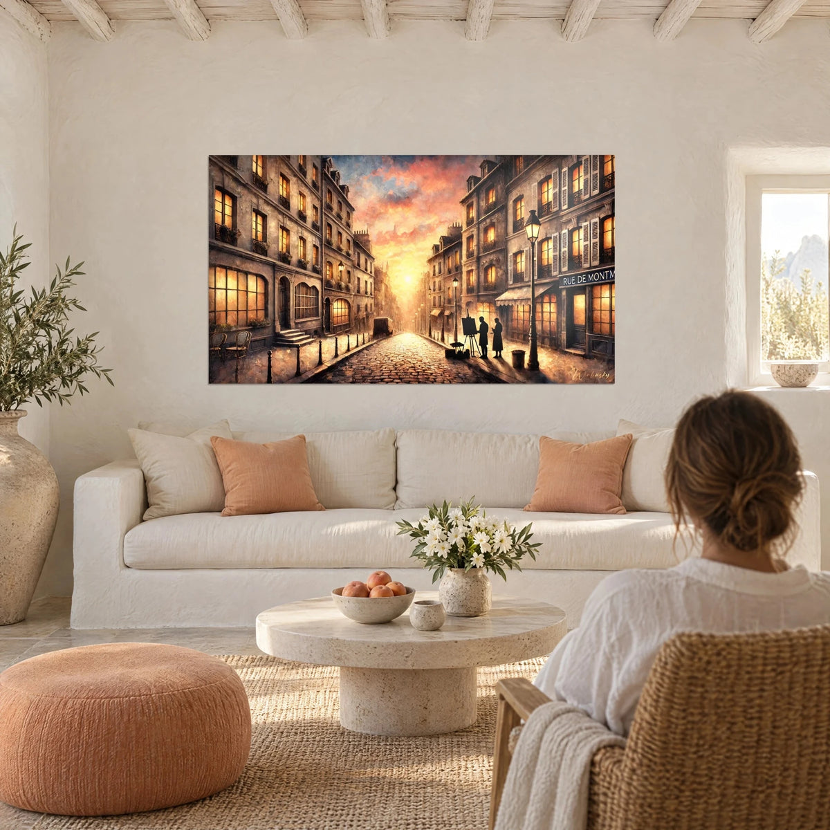 Gemälde einer Pariser Gasse mit Kopfsteinpflaster unter rosa-orangefarbenem Himmel, bernsteinfarbene Fenster, schwarze Straßenlaterne, über einem Sofa in einem hellen Wohnzimmer