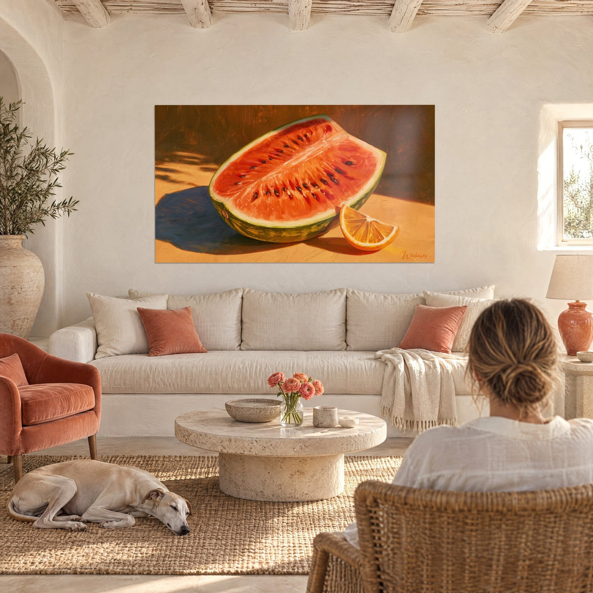 Tableau pastèque entamée à la chair vermillon, quartier d'orange et ombre bleue, au-dessus d'un canapé dans un salon lumineux