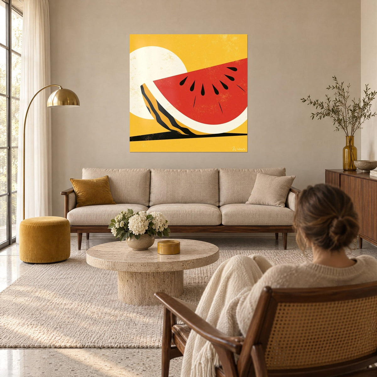 Wall art red watermelon slice with black seeds on a cream sun and yellow background, woman seen from behind, hung above a sofa in a bright living room