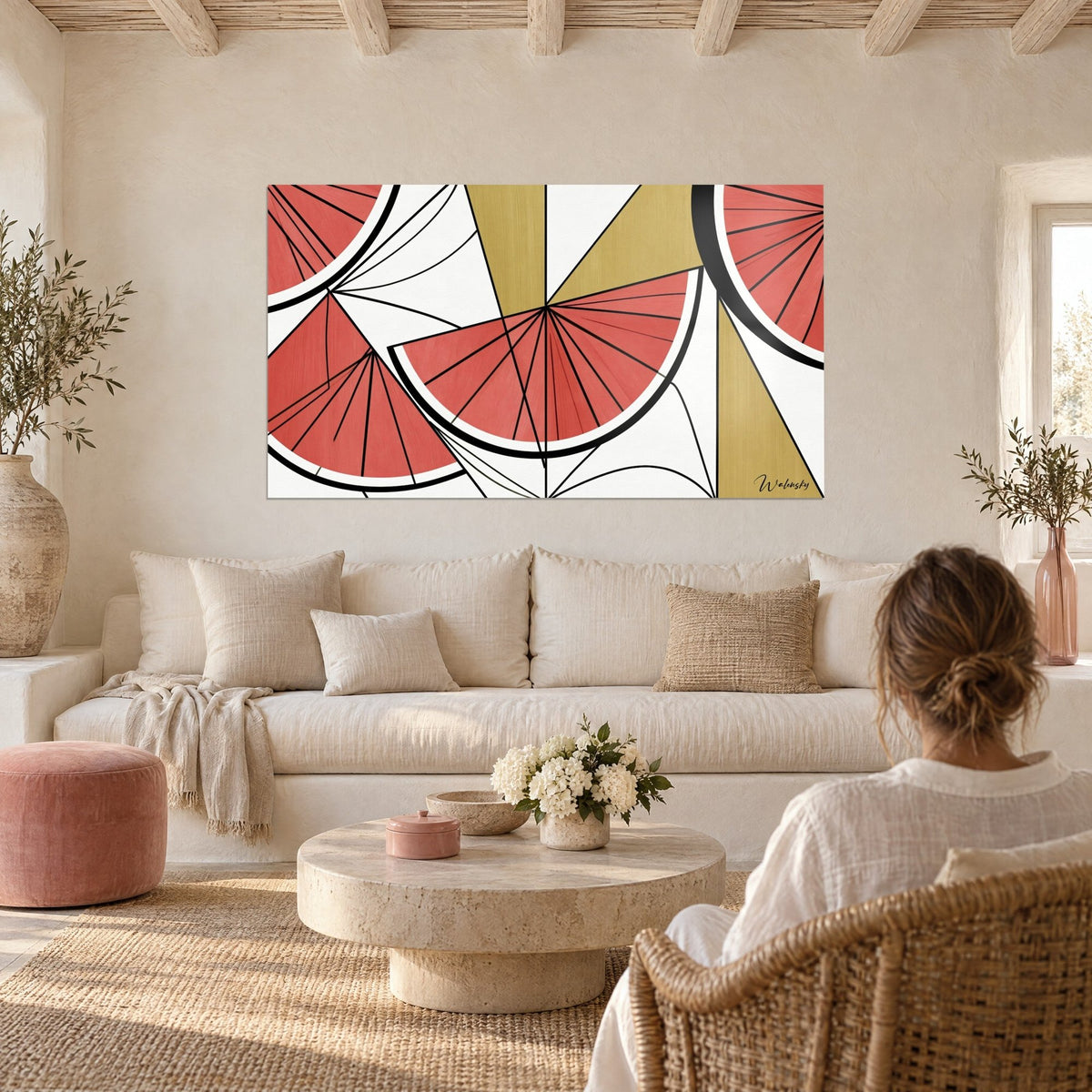 Wall art coral watermelon slices with black rays and golden triangles, woman seen from behind, above a sofa in a bright living room