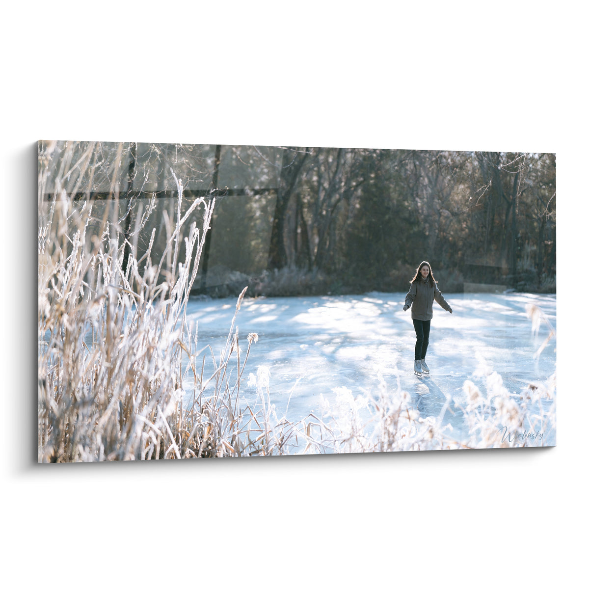 Patineuse en manteau gris glissant sur glace bleu pastel bordée de roseaux ocre givrés