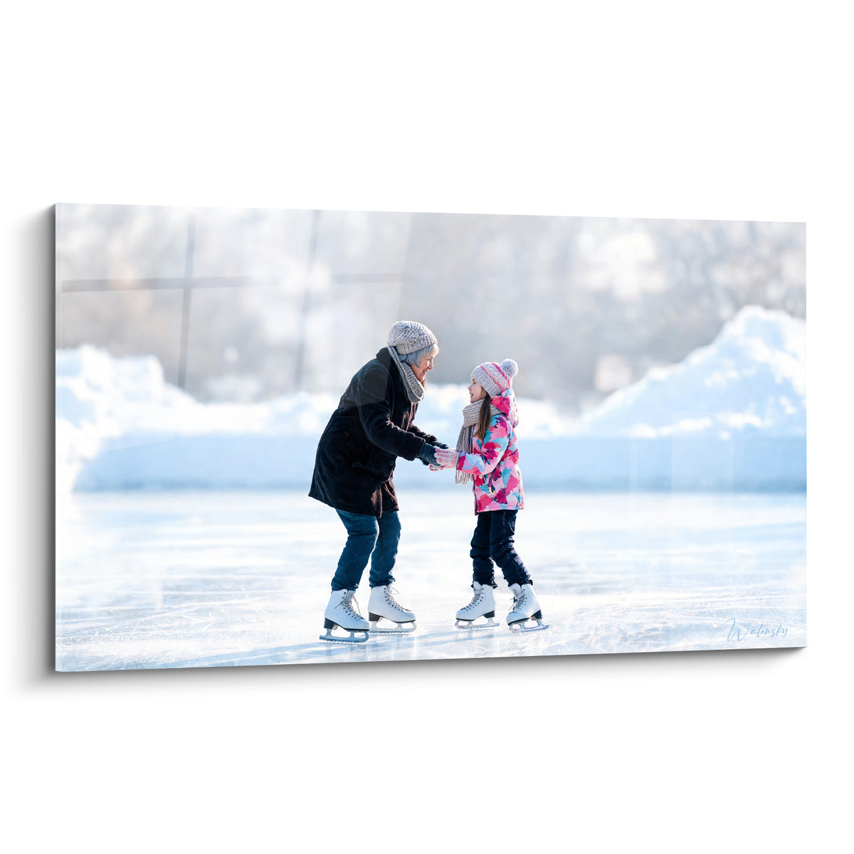 Grand-mère en manteau anthracite tenant les mains d'une fillette en veste rose sur la glace blanche