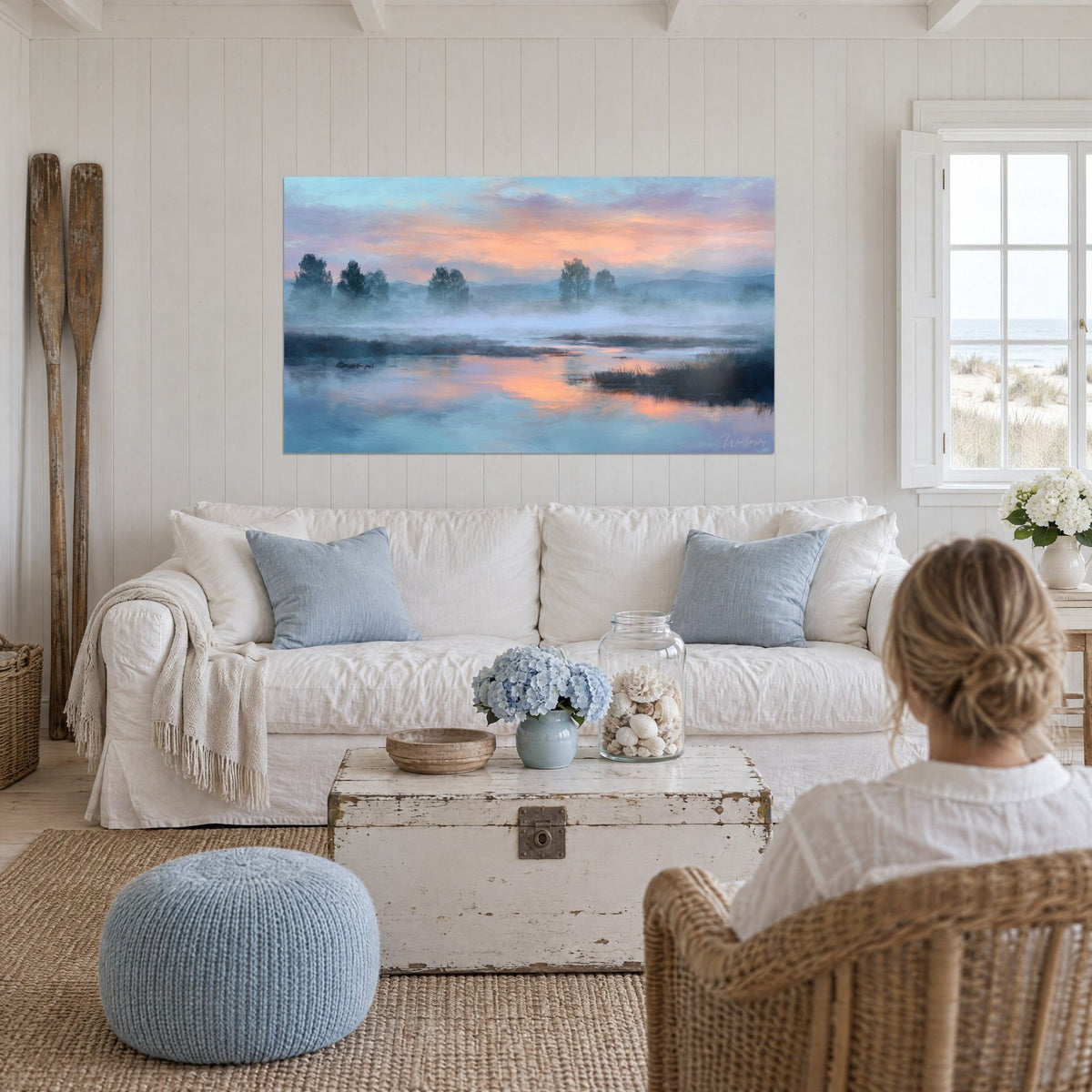 Tableau marais embrumé au lever du jour, ciel rose et orangé, eau bleutée, au-dessus d'un canapé dans un salon lumineux