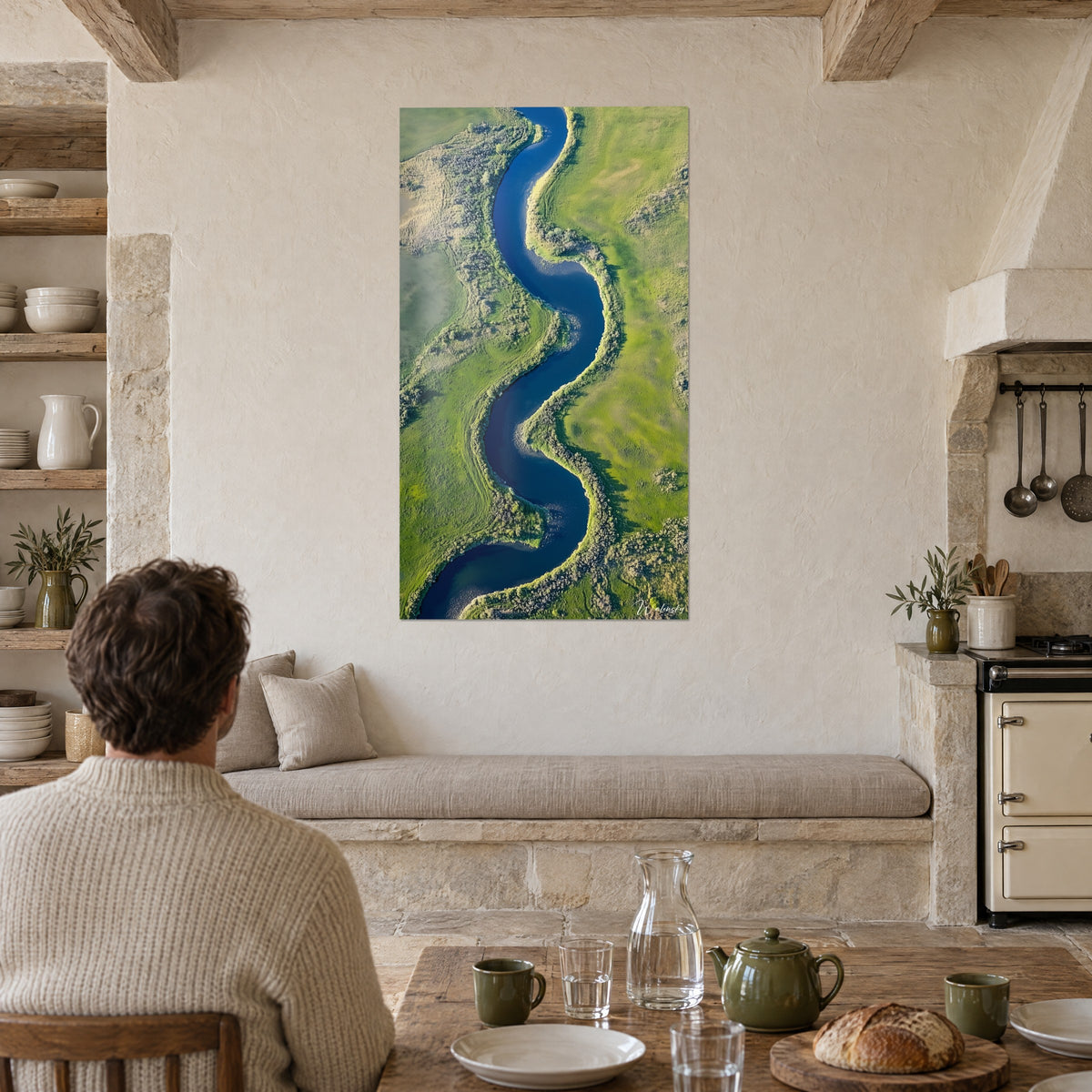 Quadro anse di un fiume azzurro tra pascoli giallo-verdi, appeso in una cucina con pietra chiara, tavolo in legno