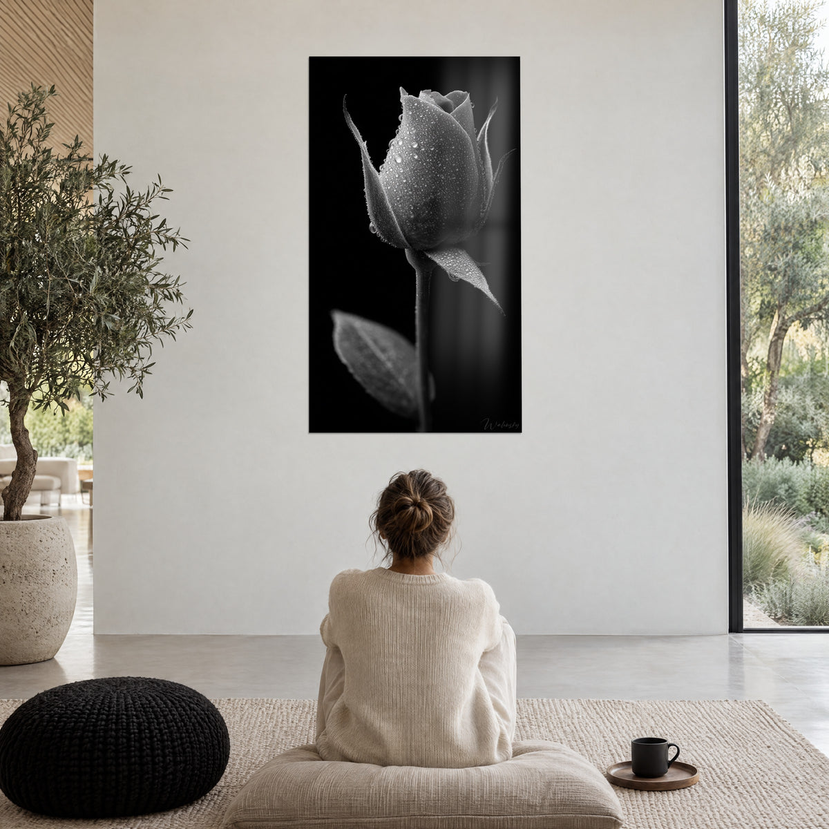 Cuadro flor de rosal entreabierta y húmeda, gris plateado sobre negro tinta, mujer de espaldas sentada en un puf, gran ventanal