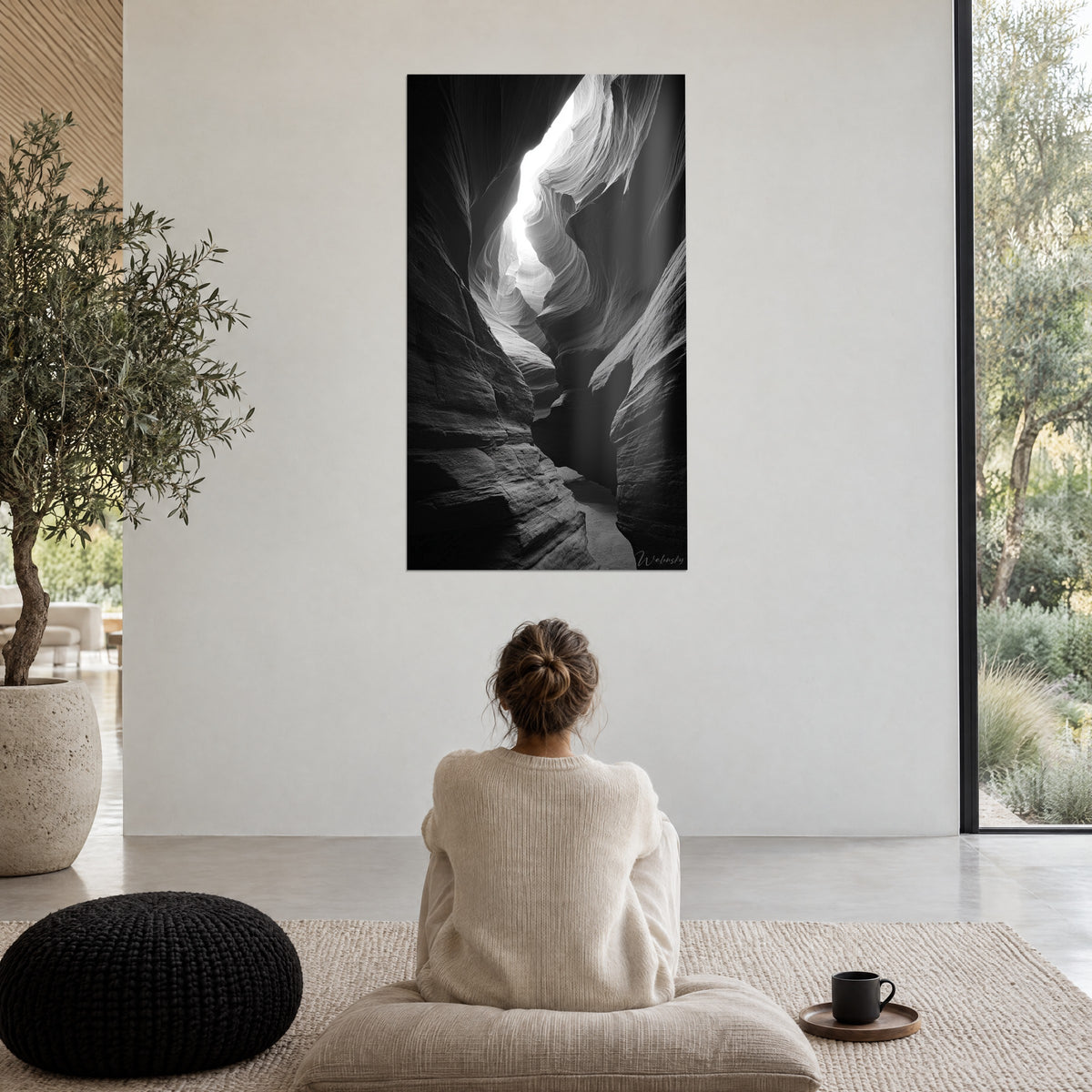 Schilderij zwart-witte zandstenen kathedraal, door de wind gevormde krommingen en een lichtbundel, zittende vrouw van achteren op een poef