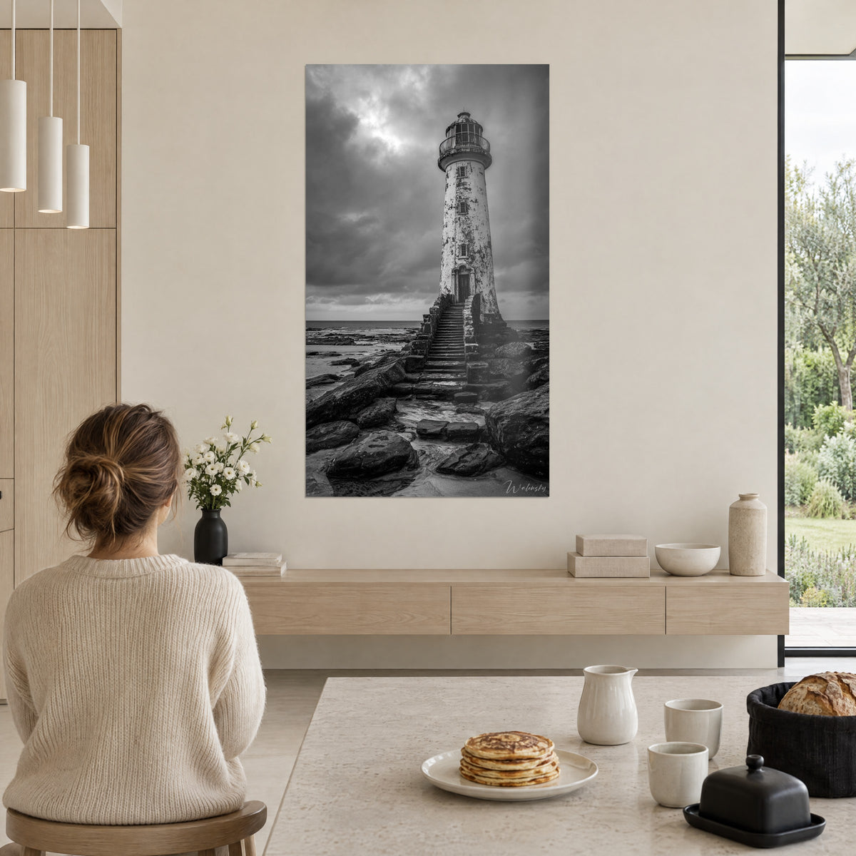 Schilderij kustlantaarn op een stenen trap, zwart-witte lucht, vrouw van achteren in een crèmekleurige trui, ontbijttafel, open leefruimte