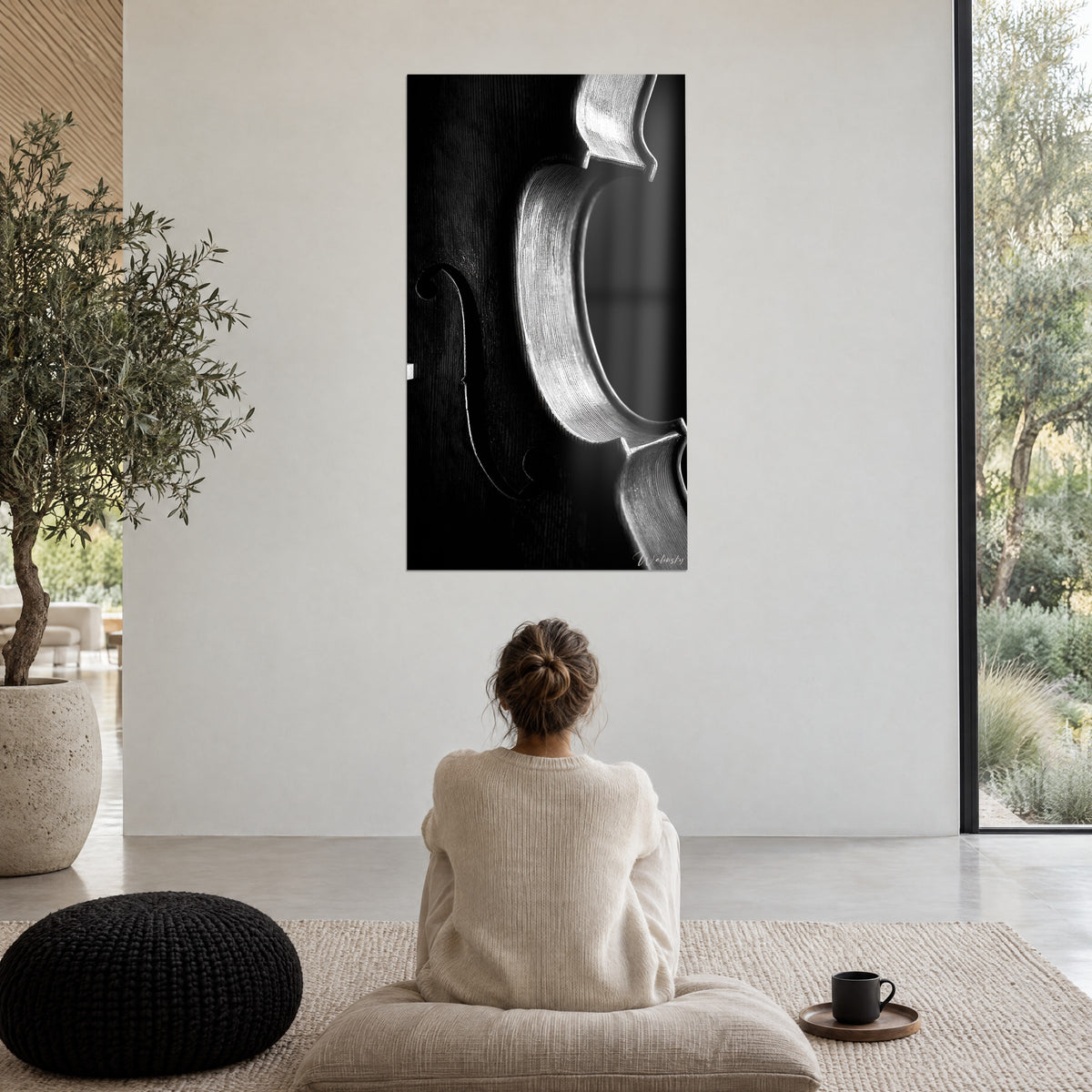 Schilderij zonder strijkstok, gesneden klankgat en zilveren vioolzijde op zwarte achtergrond, persoon van achteren mediterend op een zwarte poef, strakke woonkamer