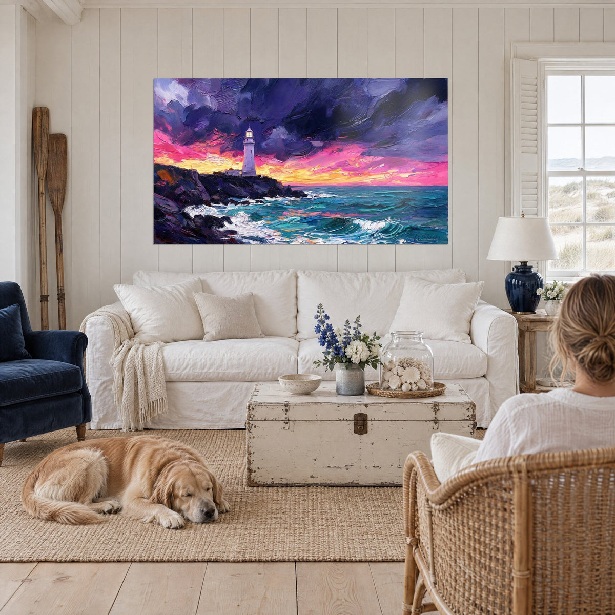 Schilderij met witte vuurtoren onder een roze en paarse lucht, turquoise schuimende zee, liggende retriever, boven een bank in een lichte woonkamer