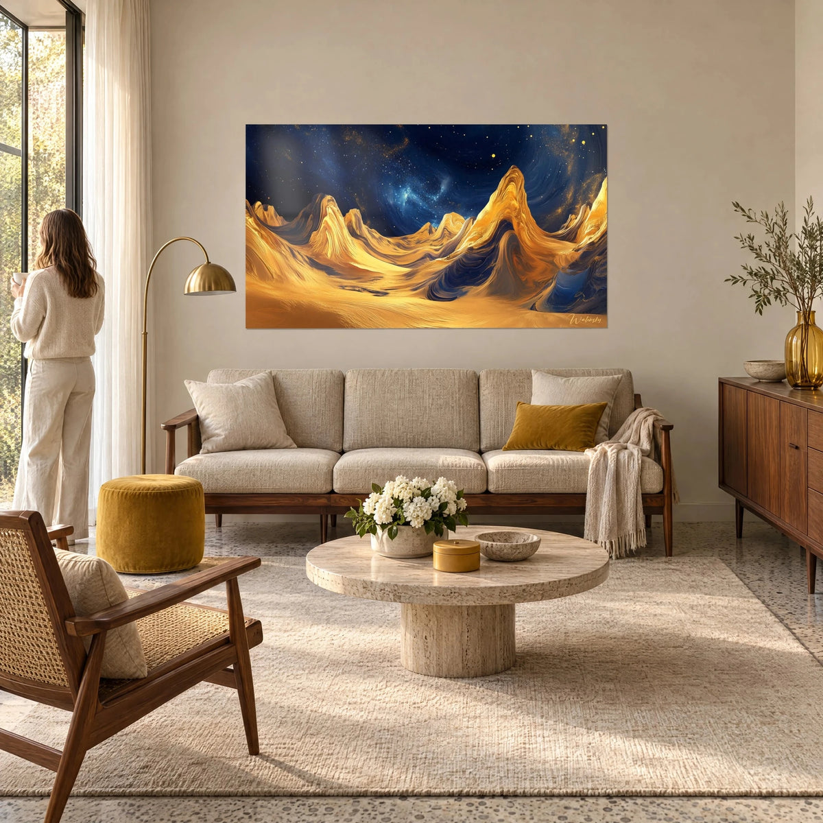 Wall art golden sculpted dunes under a starry midnight-blue sky, woman seen from behind, above a sofa in a bright living room