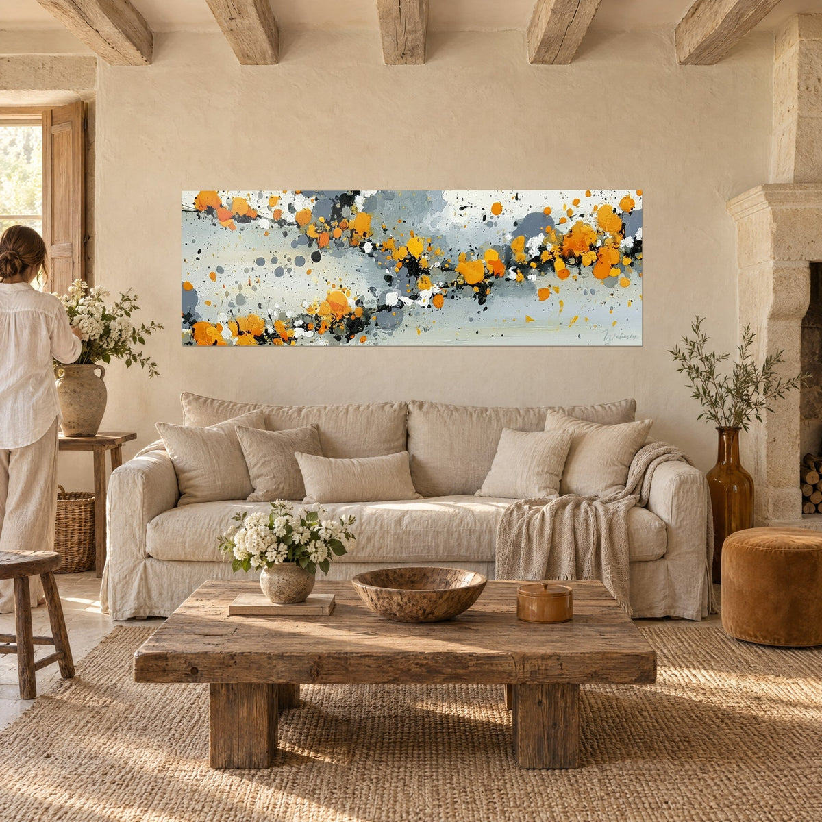 Wall art with a constellation of vivid orange splashes on a pearl grey background, streaked with black drops, above a sofa in a bright living room