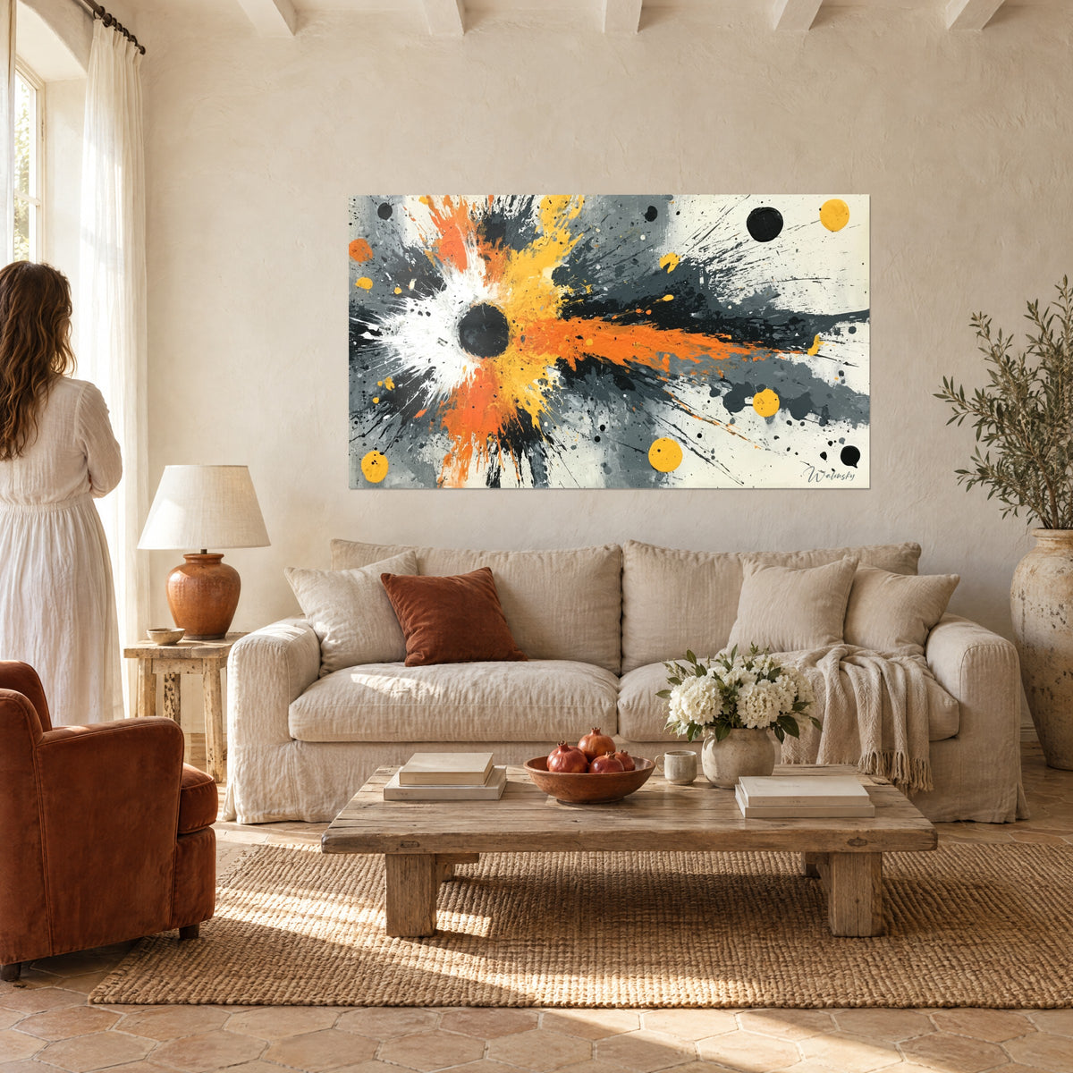 Tableau trou noir éclaté en jaune et orange, éclaboussures grises, femme de dos, au-dessus d'un canapé dans un salon lumineux