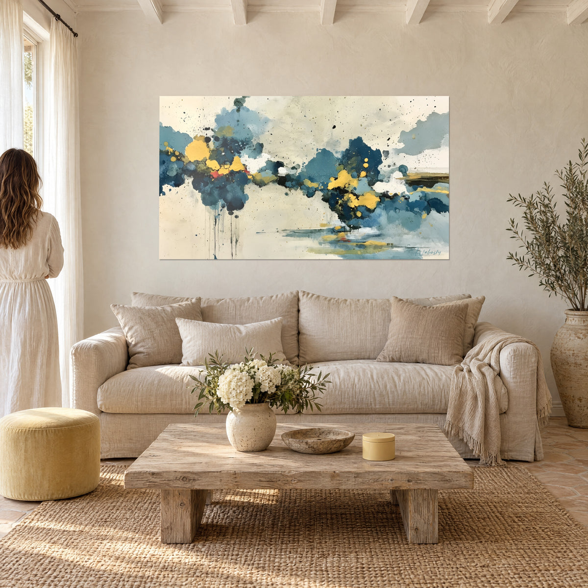 Tableau abstrait de nuages bleu marine éclaboussés d'ocre doré, une femme de dos, au-dessus d'un canapé dans un salon lumineux