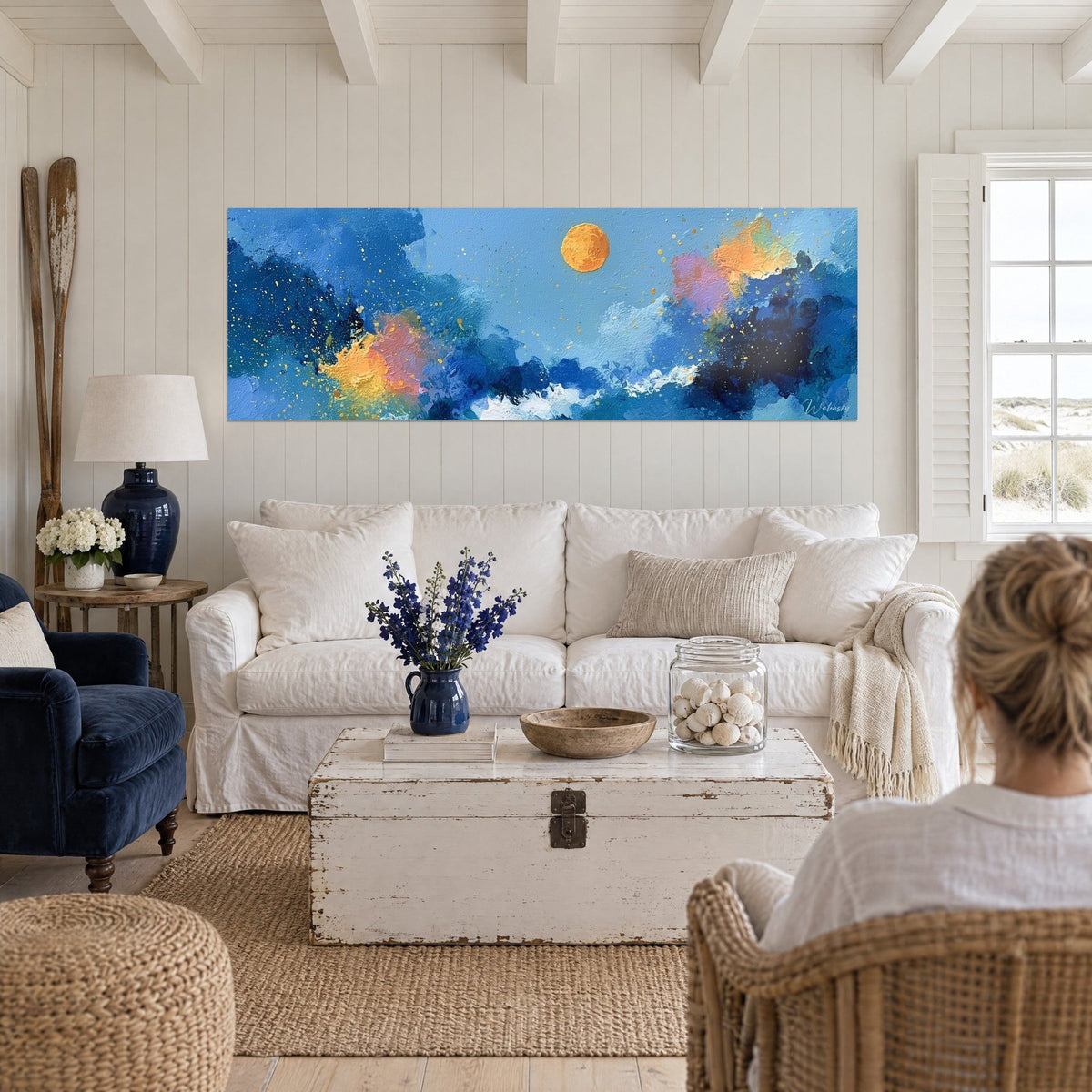 Wall art orange moon over navy blue waves, golden splashes, two women seen from behind, above a sofa in a bright living room