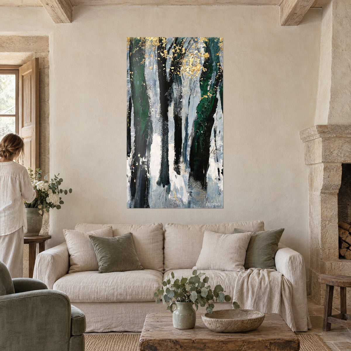 Tableau troncs d'arbres noirs et verts piquetés de feuilles d'or sur fond bleu-gris, au-dessus d'un canapé dans un salon lumineux