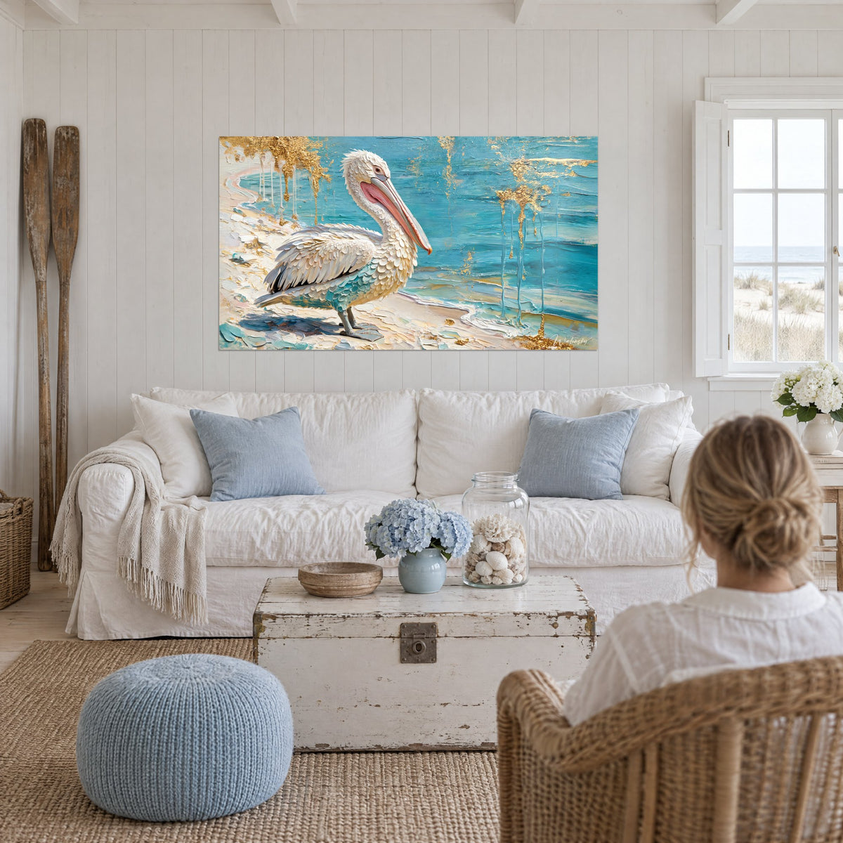Tableau pélican blanc au long bec rose posé sur sable ivoire, mer turquoise et coulures dorées, au-dessus d'un canapé dans un salon lumineux