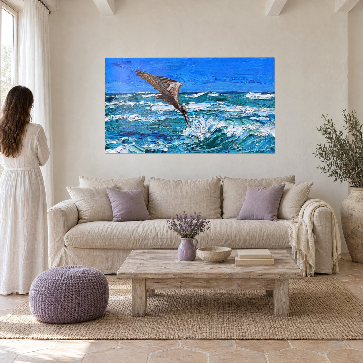 Tableau pélican brun plongeant, ailes déployées sur un ciel bleu cobalt et des vagues turquoise, au-dessus d'un canapé dans un salon lumineux