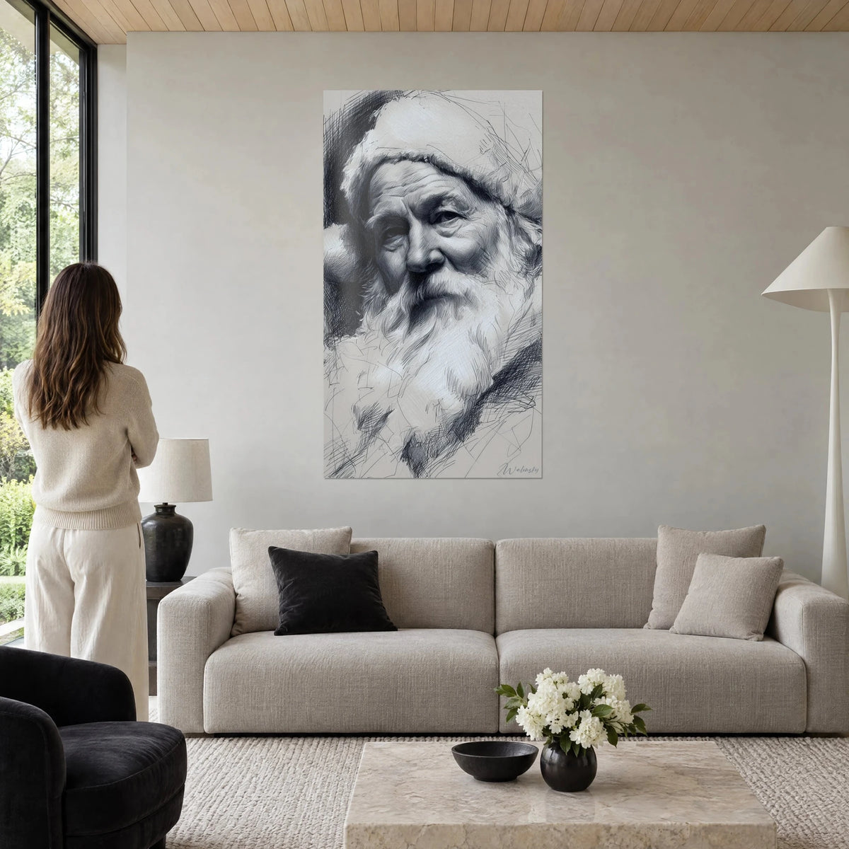 Cuadro de Papá Noel a lápiz, barba blanca y gorro peludo gris antracita, mujer de espaldas, encima de un sofá en un salón luminoso