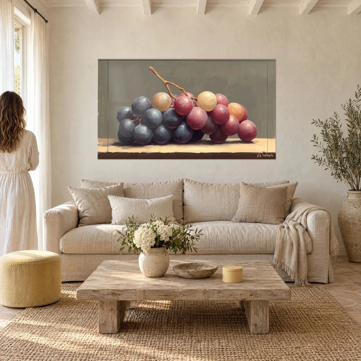 Tableau grappe de raisins bleu nuit et rose bordeaux sur fond vert-gris, une femme de dos, au-dessus d'un canapé dans un salon lumineux
