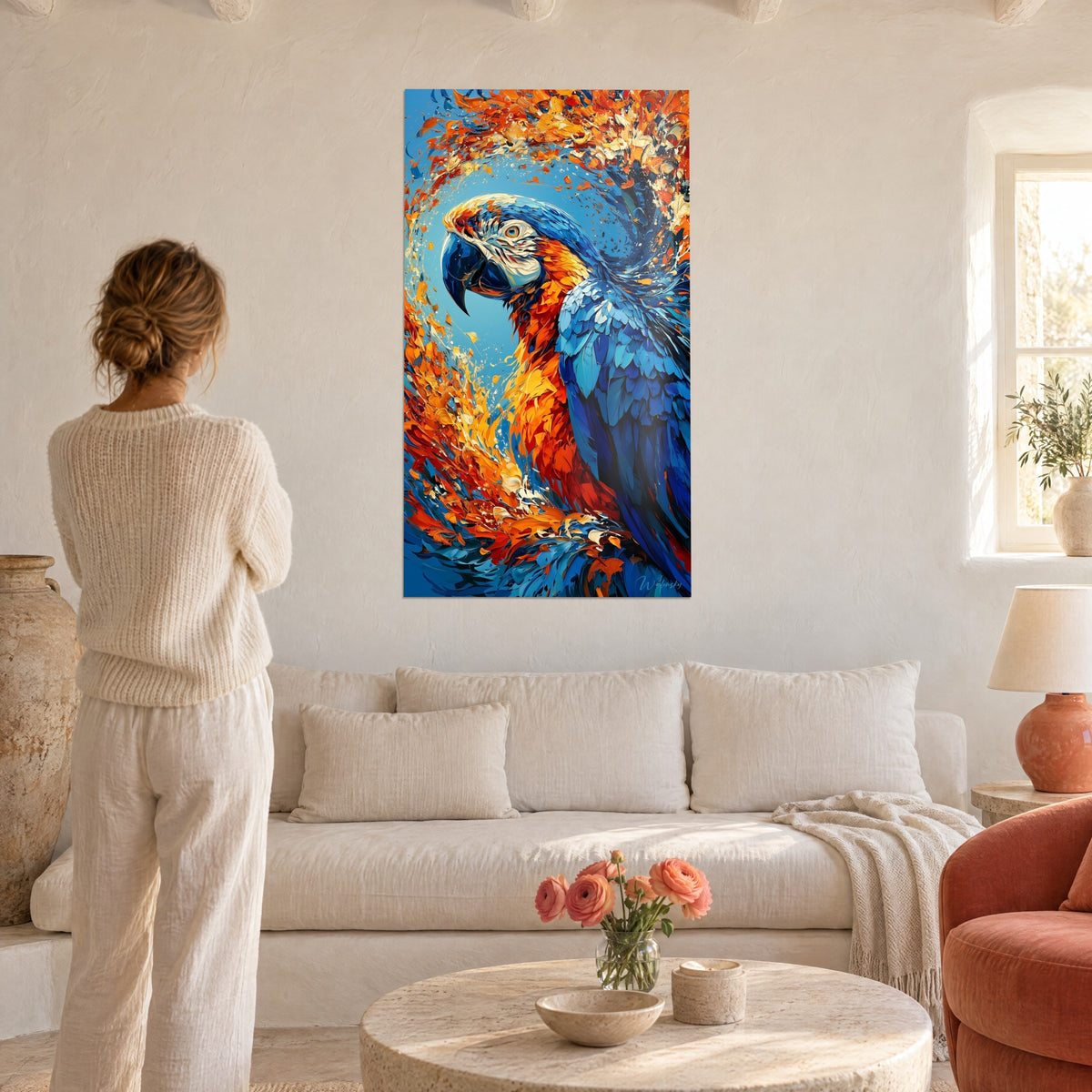 Tableau ara bleu cobalt au bec noir, plumes orange en spirale, une femme de dos au-dessus d'un canapé dans un salon lumineux
