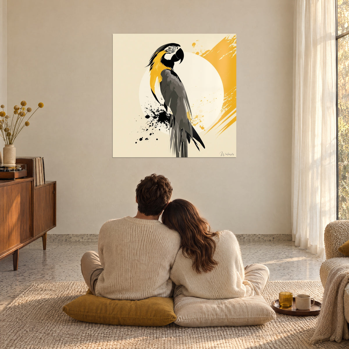 Tableau ara perché, queue gris charbon effilée et pinceau jaune d'or en diagonale, face à un couple enlacé sur des coussins moutarde, grande baie vitrée