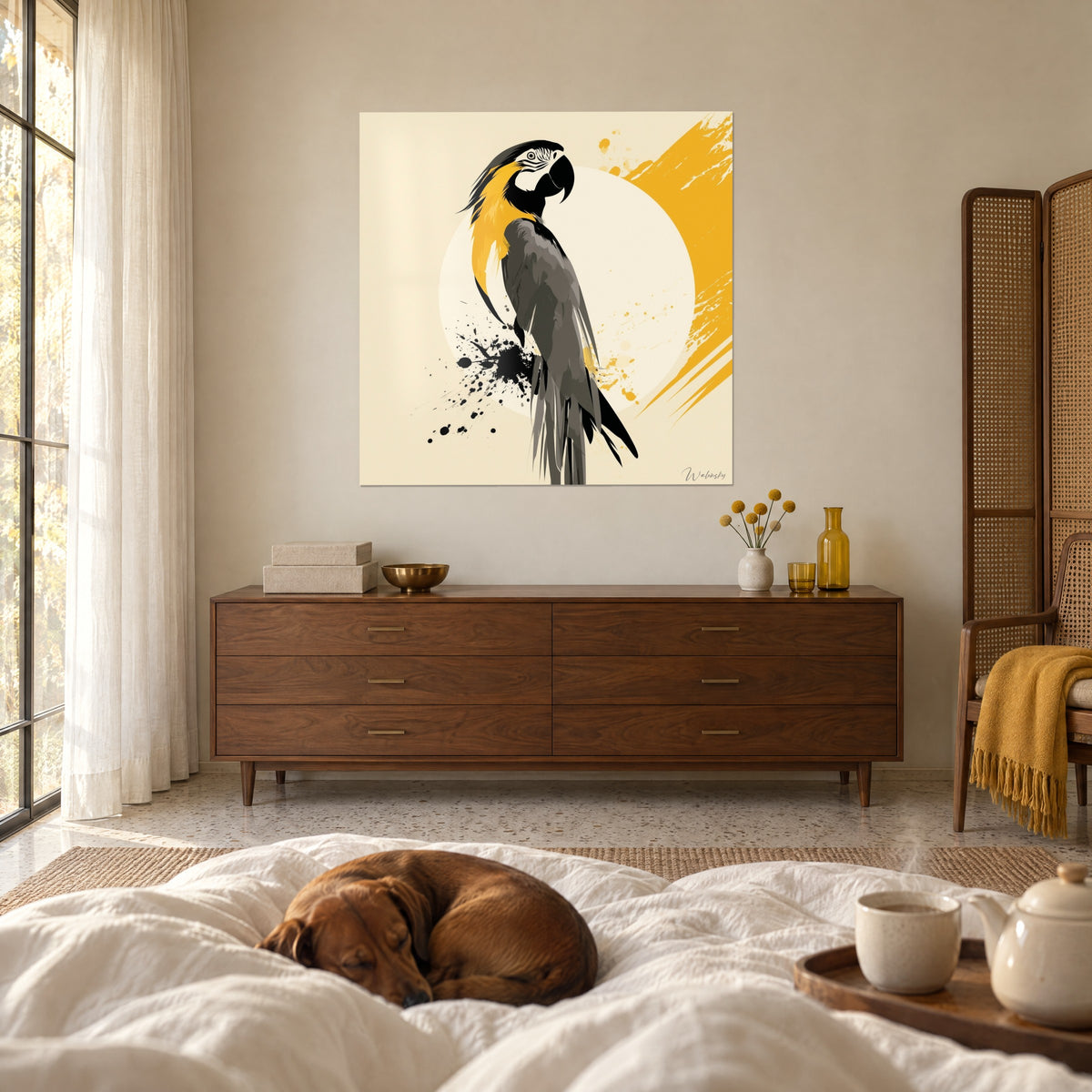 Tableau volatile aux plumes anthracite et or posé sur un disque crème, face à un dachshund endormi sur un lit blanc, au-dessus d'un lit dans une chambre claire