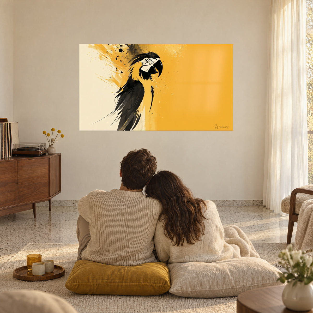 Wall art yellow and black macaw with ink splashes, facing a couple embracing from behind, seated on mustard and cream cushions