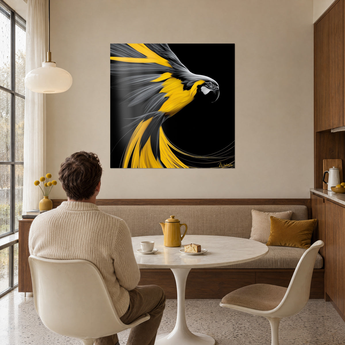 Wall art of a vivid yellow and pearl-grey macaw, white-ringed eye, admired by a man seated at the table near the window in a sunlit living room