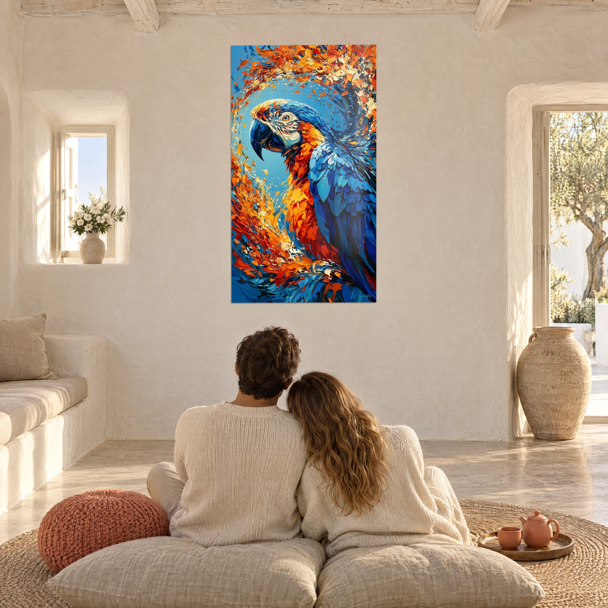 Tableau vortex de plumes orange brûlé sur fond bleu ciel, un couple de dos sur des coussins, mur blanc de maison grecque