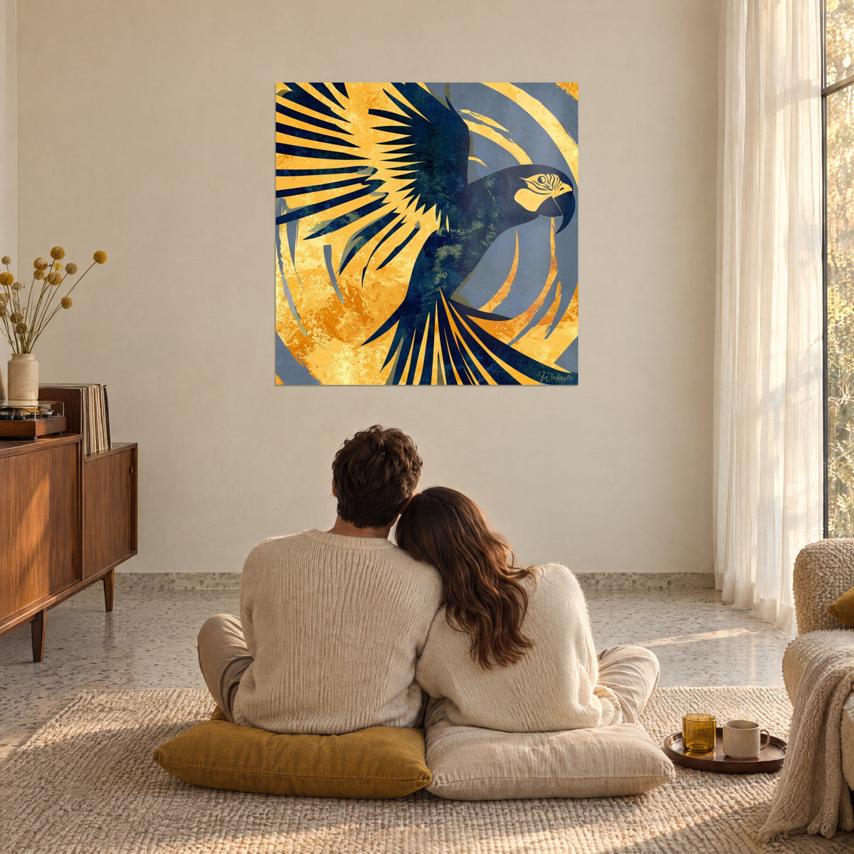 Tableau envol d'oiseau exotique, plumage bleu profond sur fond orangé doré, couple de dos assis au sol, salon baigné de soleil
