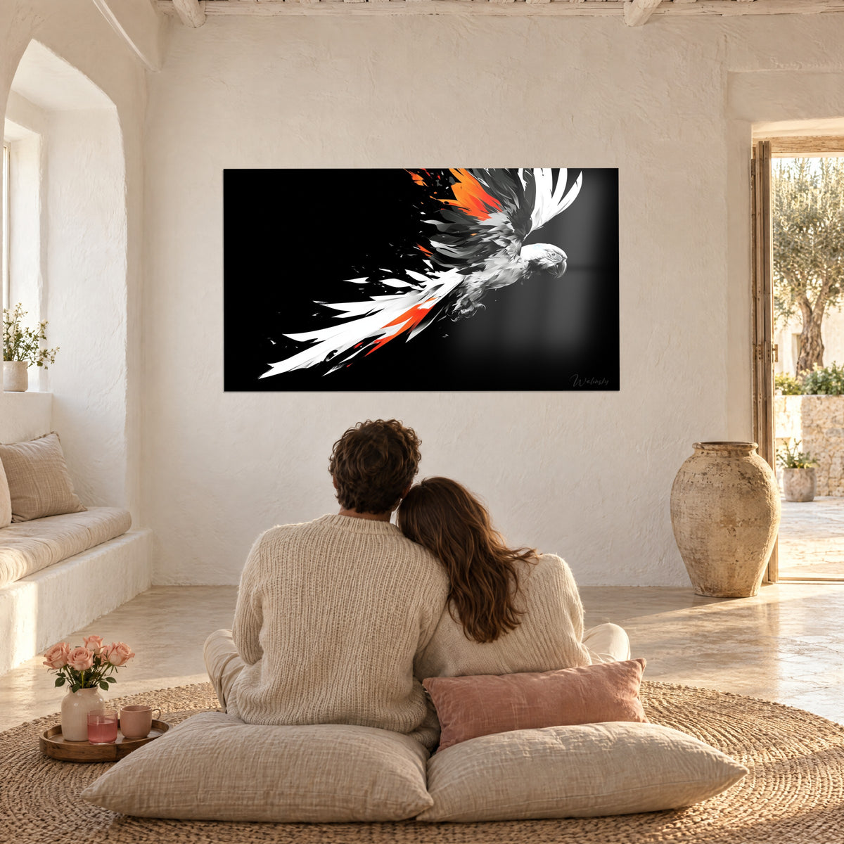 Wall art of a white bird in flight streaked with black and highlighted in orange on a black background, a couple seated with their backs to the viewer on cushions in the living room