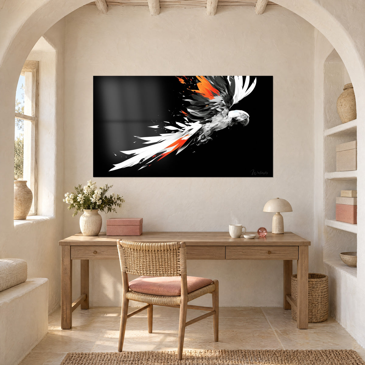 Wall art of a dazzling macaw, white layered tail and bold orange strokes on a black background, above a light wood desk next to a rattan armchair