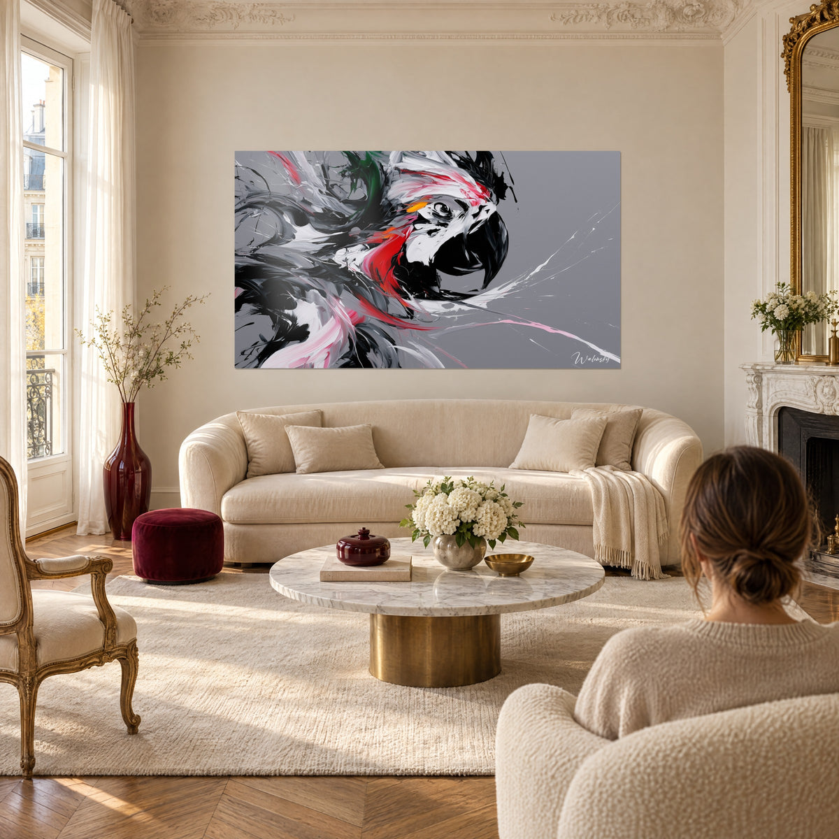 Tableau ara noir et blanc au bec entrouvert, plumes rouges et fond gris, femme de dos au-dessus d'un canapé dans un salon lumineux