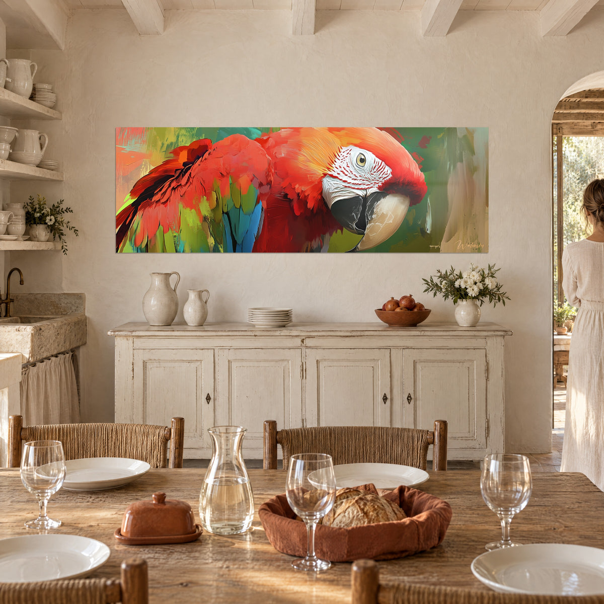 Cuadro gran guacamayo en pintura gruesa naranja y verde oliva, mujer de espaldas junto a una mesa puesta en una masía