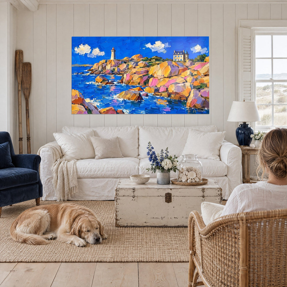 Schilderij met een witte vuurtoren op roze en okerkleurige granieten rotsen, kobaltblauwe zee, boven een bank in een lichte woonkamer