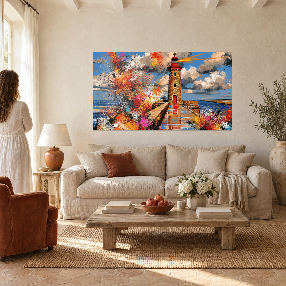 Quadro faro di mattoni rossi e ocra schizzato di arancio vivo su cielo azzurro, donna di spalle, sopra un divano in un soggiorno luminoso