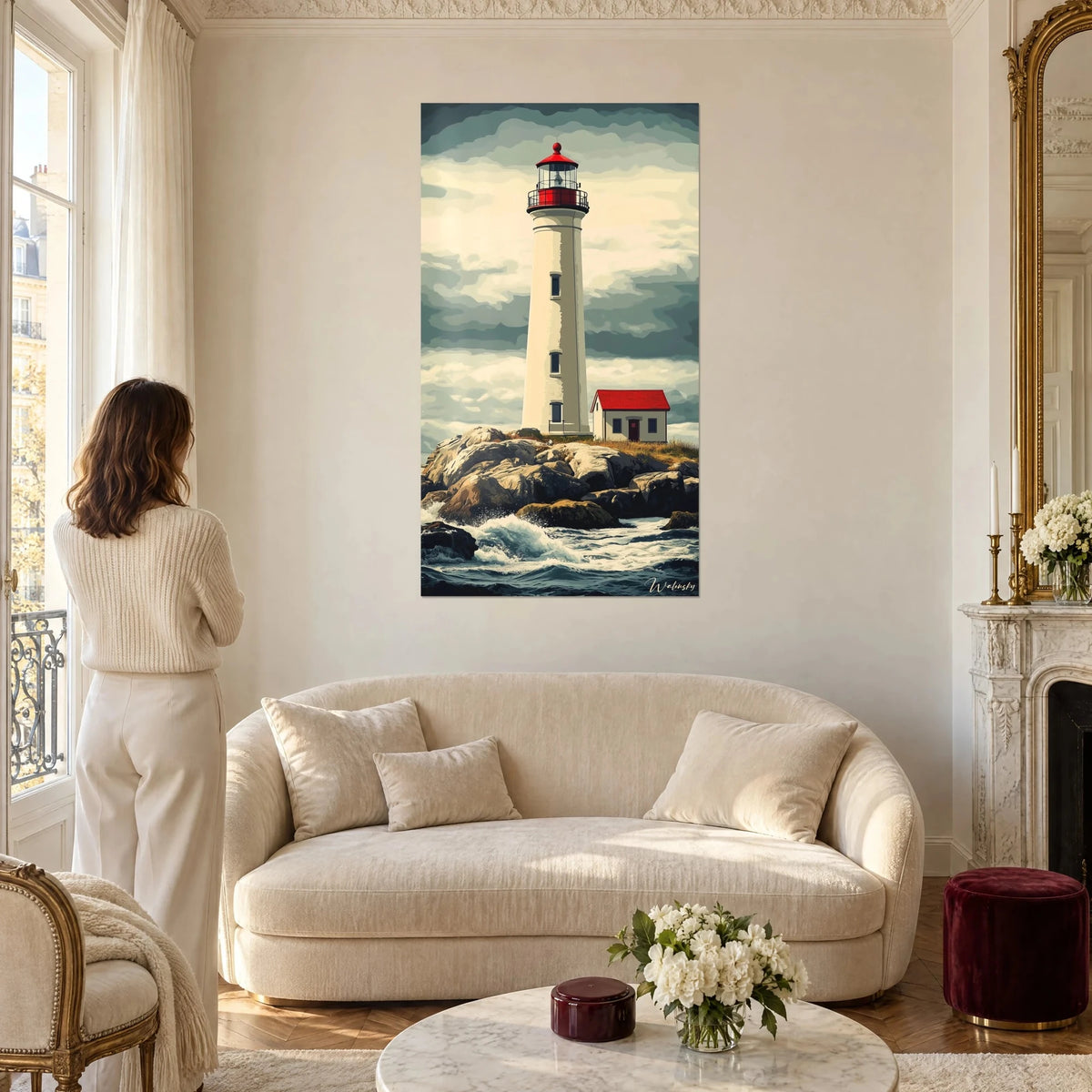 Cuadro faro blanco con cúpula roja sobre rocas bajo un cielo gris, mujer de espaldas, encima de un sofá en un salón luminoso