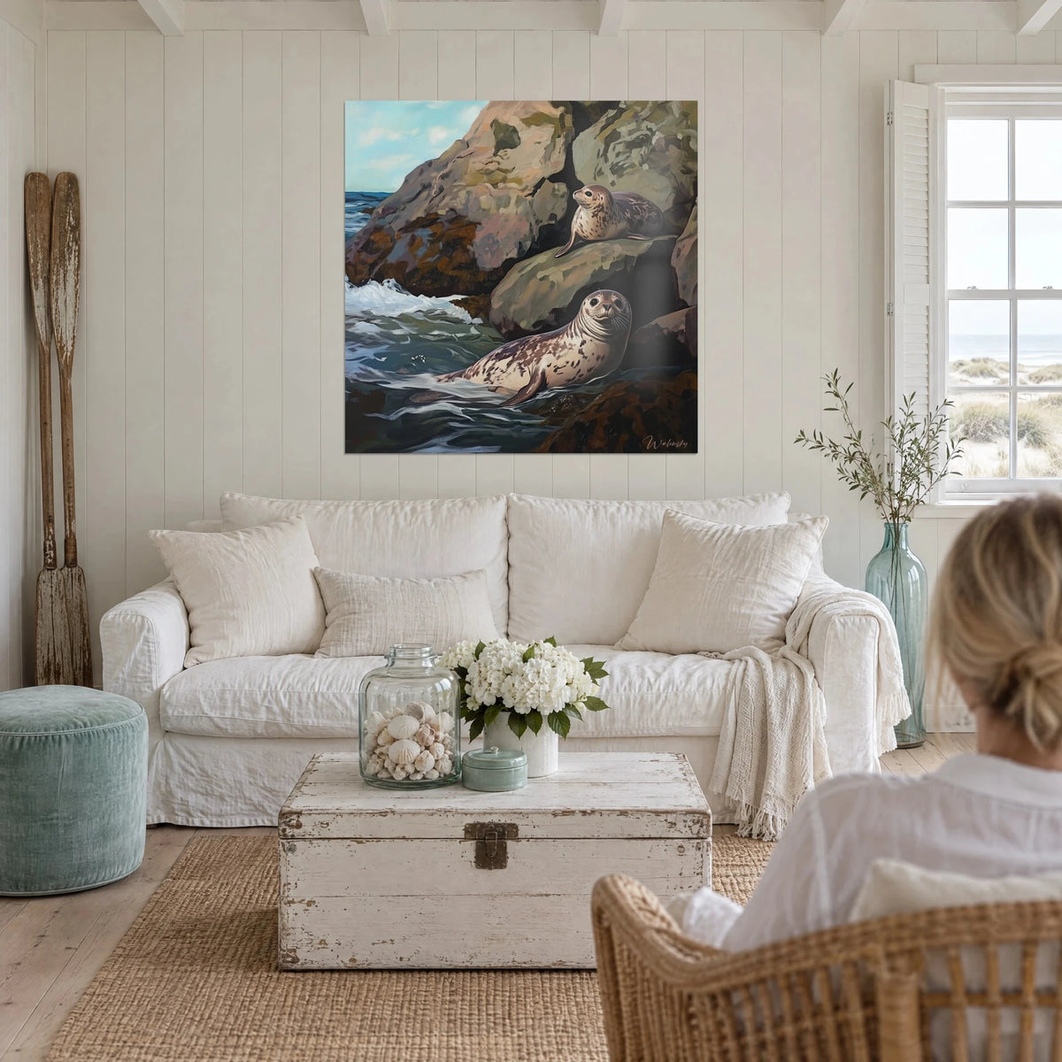 Tableau phoques tachetés au repos sur un rocher ocre, mer verte écumante, personne de dos, au-dessus d'un canapé dans un salon lumineux
