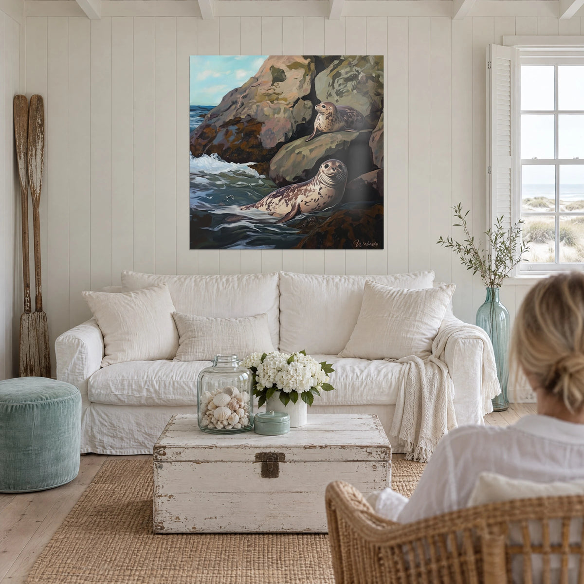 Schilderij gevlekte zeehonden die rusten op een oker rots, schuimende groene zee, persoon van achteren, boven een bank in een lichte woonkamer
