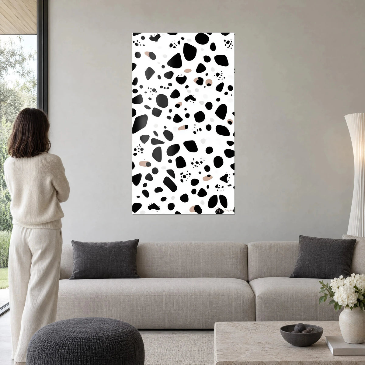 Quadro con motivo dalmata, macchie nere profonde su fondo bianco, due tocchi taupe, sopra un divano in un soggiorno luminoso