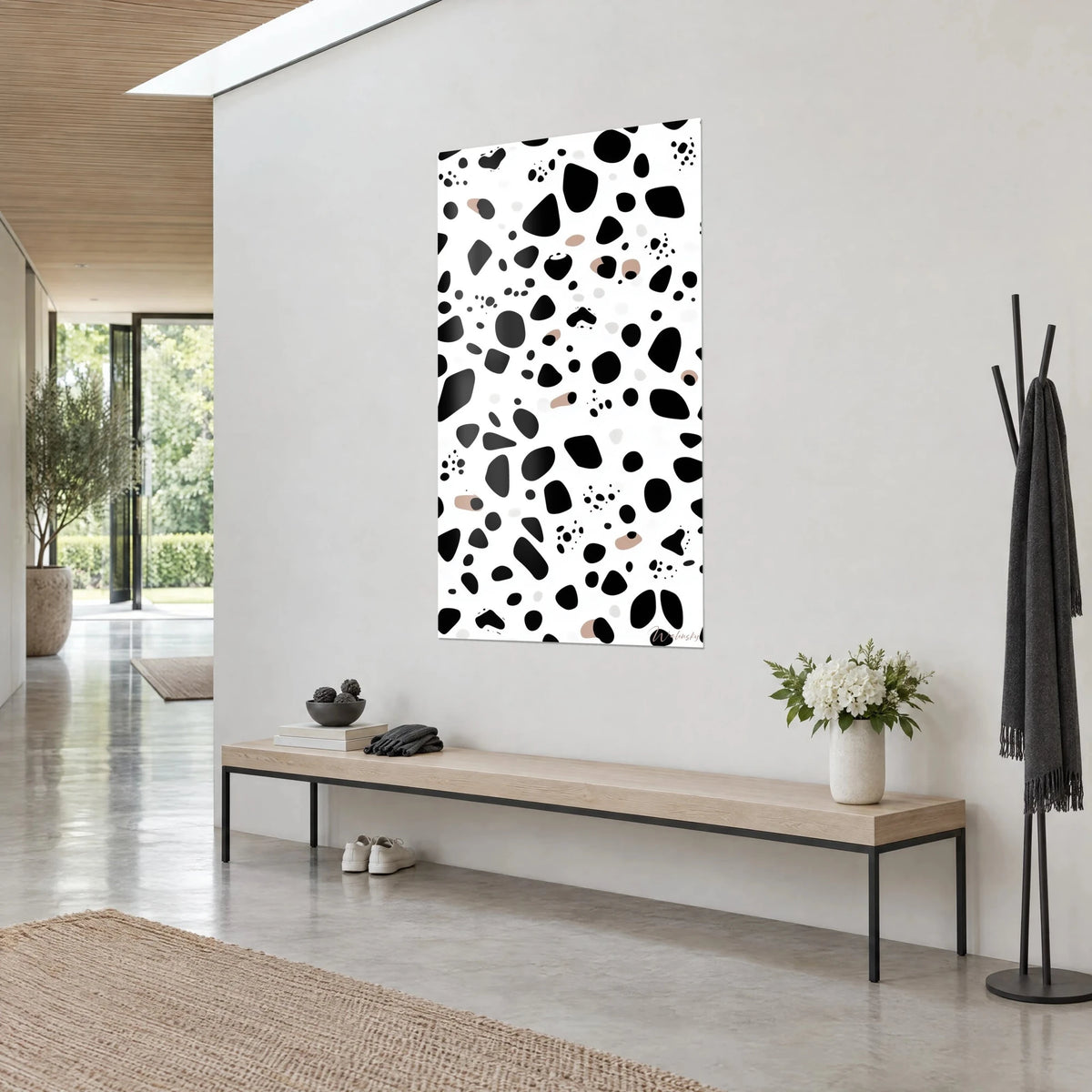 Quadro con pietre nere fluttuanti punteggiate di pois sottili, fondo bianco e riflessi rosa-beige, parete grigia, panca in legno, ingresso luminoso