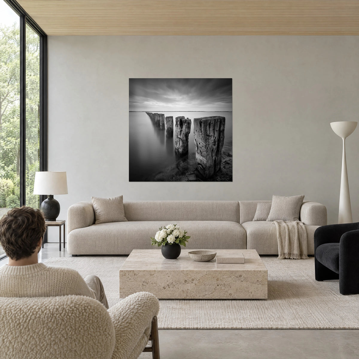 Tableau pieux en bois rongés par le sel, gris anthracite et blanc nacré, plongeant dans l'eau lisse, au-dessus d'un canapé dans un salon lumineux