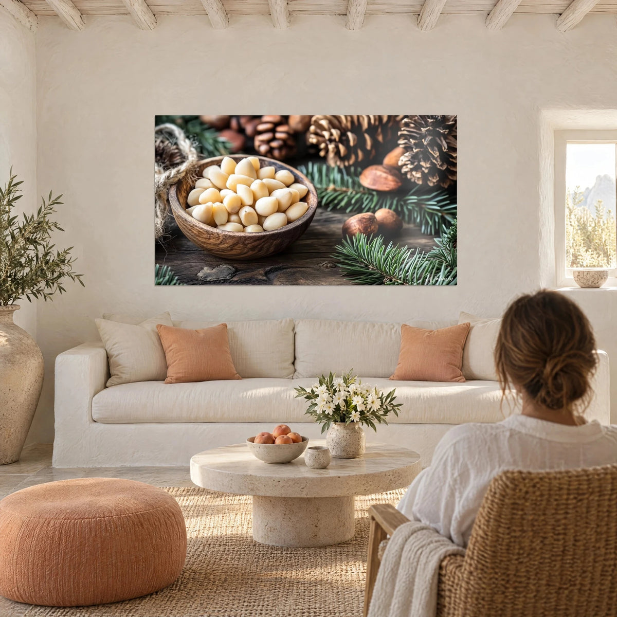 Schilderij van gepelde pijnboompitten in een houten kom, ivoor en bruin, een vrouw van achteren boven een bank in een lichte woonkamer