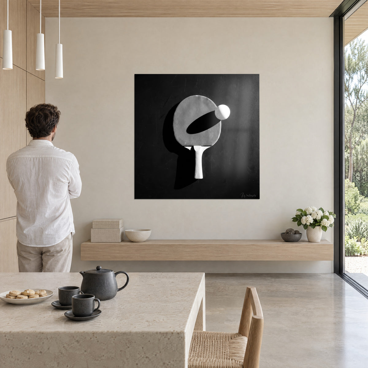 Μονοχρωματικός πίνακας ping-pong με λευκή ξύλινη λαβή και τεράστια μαύρη σκιά, απέναντι από άντρα με λευκό πουκάμισο σε ανοιχτό καθιστικό