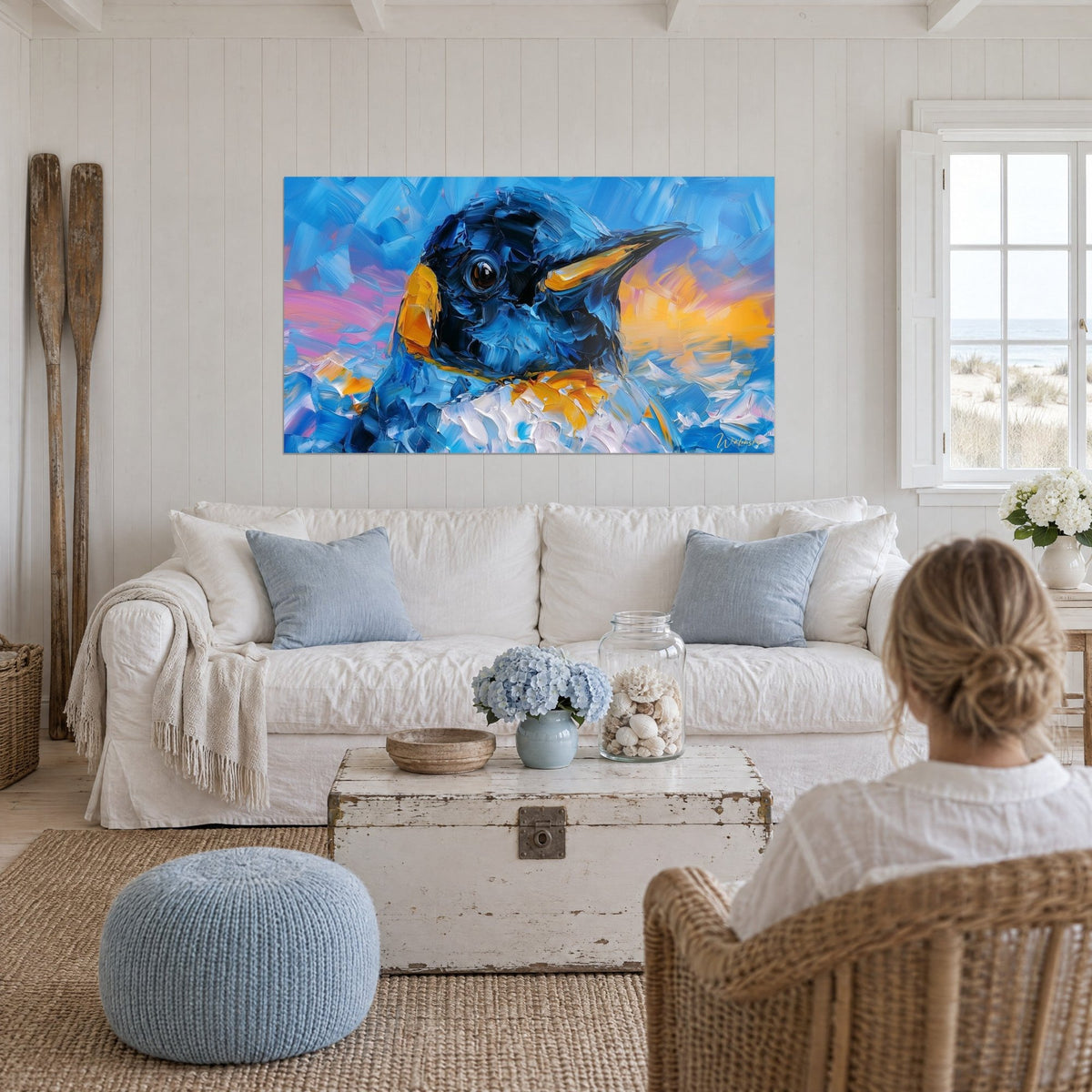 Schilderij pinguïn in kobaltblauw met bruin oog, oranjegele snavel en roze lucht, boven een bank in een lichte woonkamer