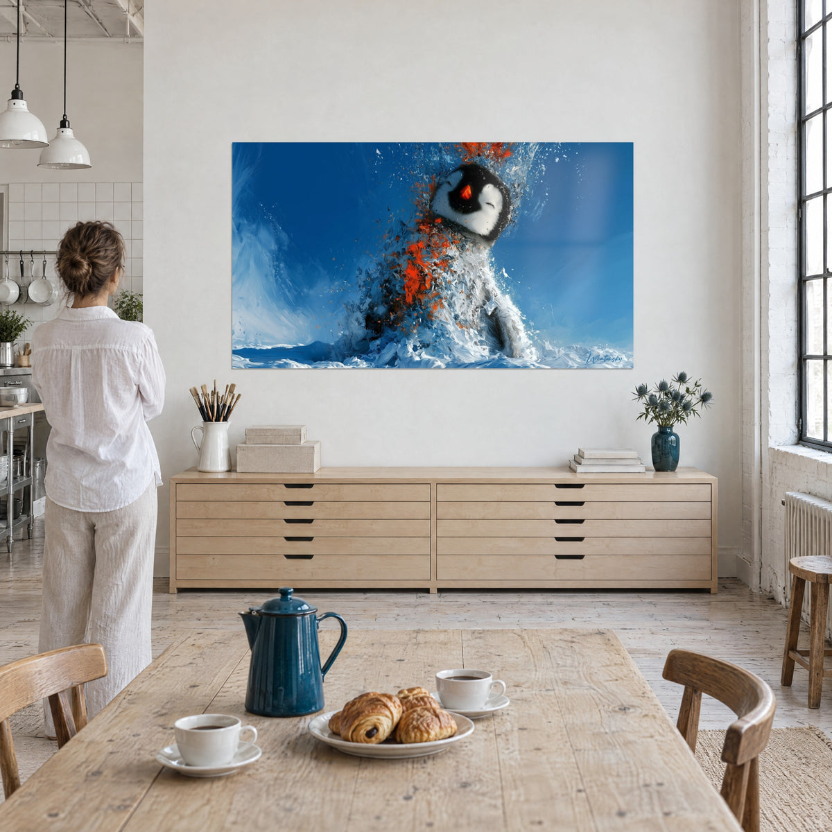 Tableau oiseau des glaces au bec orange, tête noire et blanche, éclaboussures bleu azur, regardé par une femme de dos près d'une table de loft