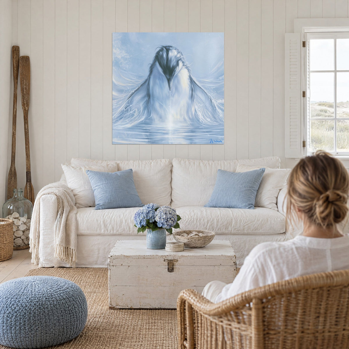 Schilderij pinguïn in zacht lichtblauw die zijn snavel in het water dompelt, witte en leikleurige veren, boven een bank in een lichte woonkamer
