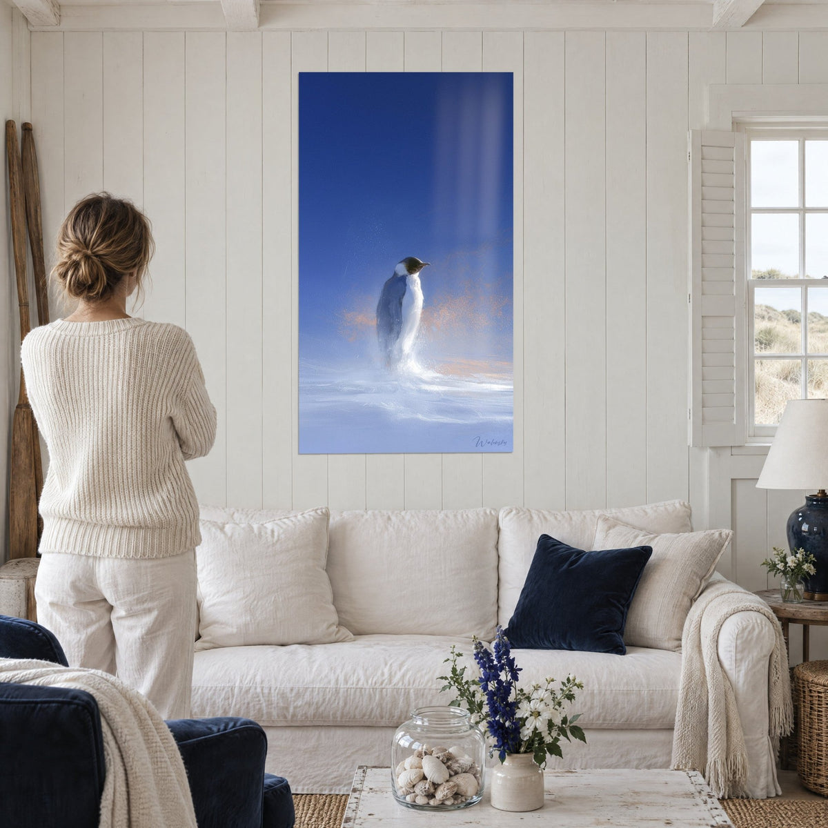 Gemälde Kaiserpinguin im Profil im Schneesturm, marineblauer Himmel und weißer Pulverschnee, über einem Sofa in einem hellen Wohnzimmer