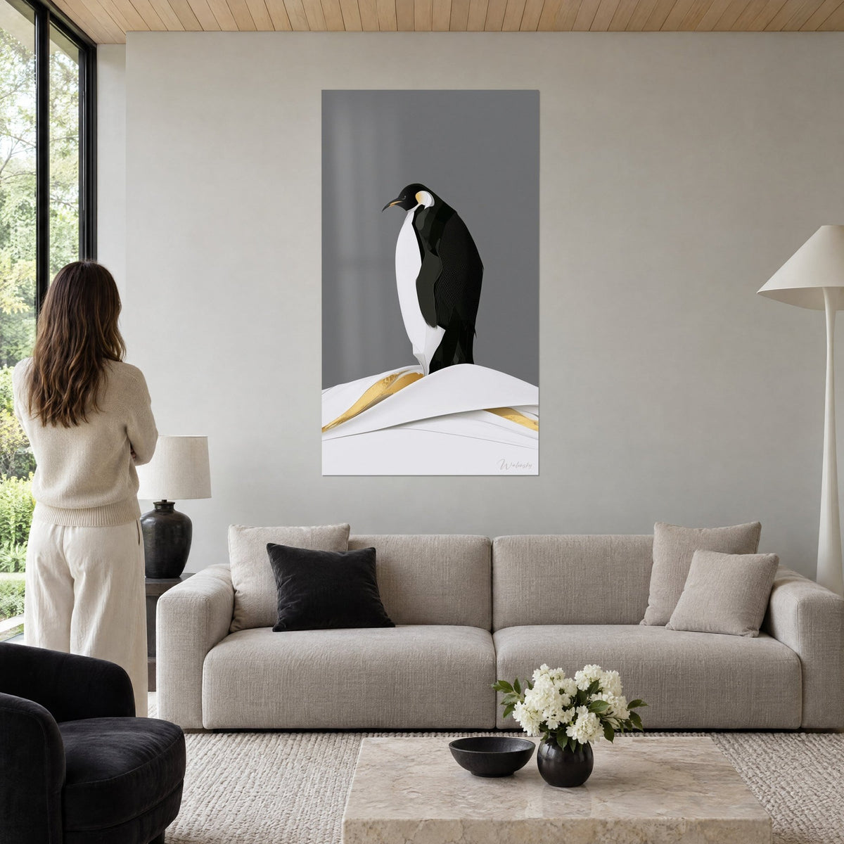 Gemälde Pinguin in Schwarz-Weiß, aufrecht auf einer schneeweißen Düne, goldene Linien, grauer Hintergrund, über einem Sofa in einem hellen Wohnzimmer