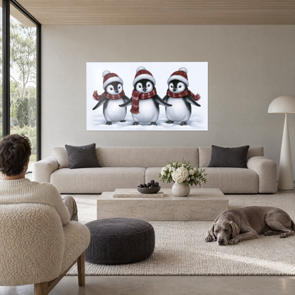 Schilderij drie pinguïnjongen met rode mutsen en geruite sjaals, zwart-wit verenkleed, boven een bank in een lichte woonkamer